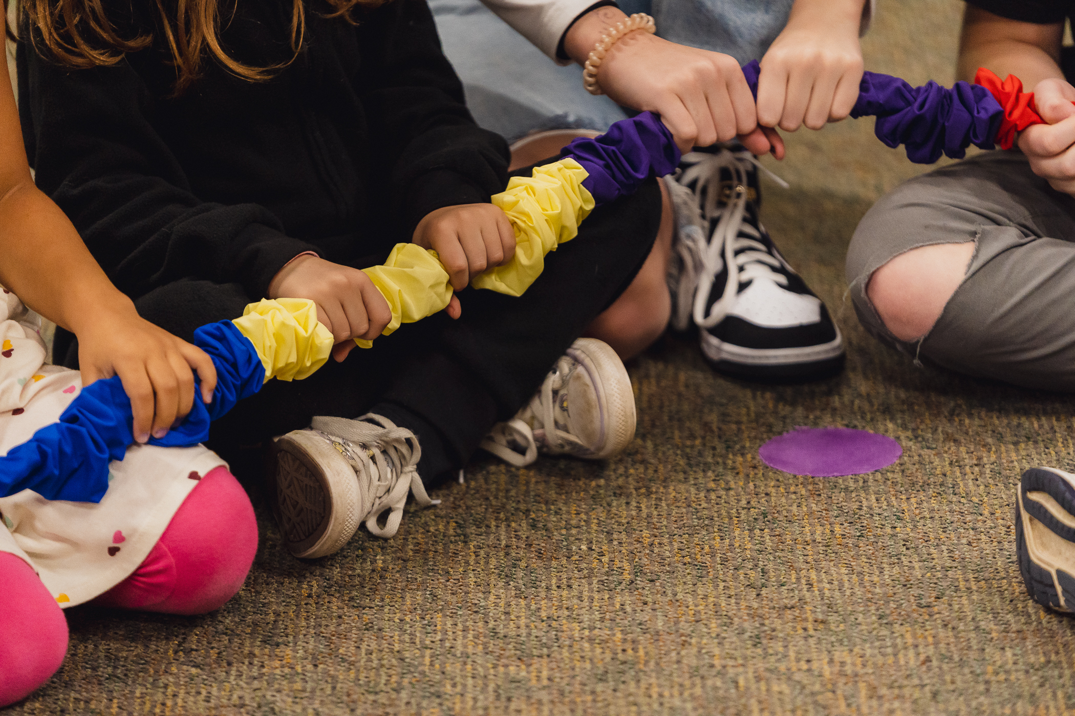 Small hands grip a colorful stretchy band together during a Kazoo movement game