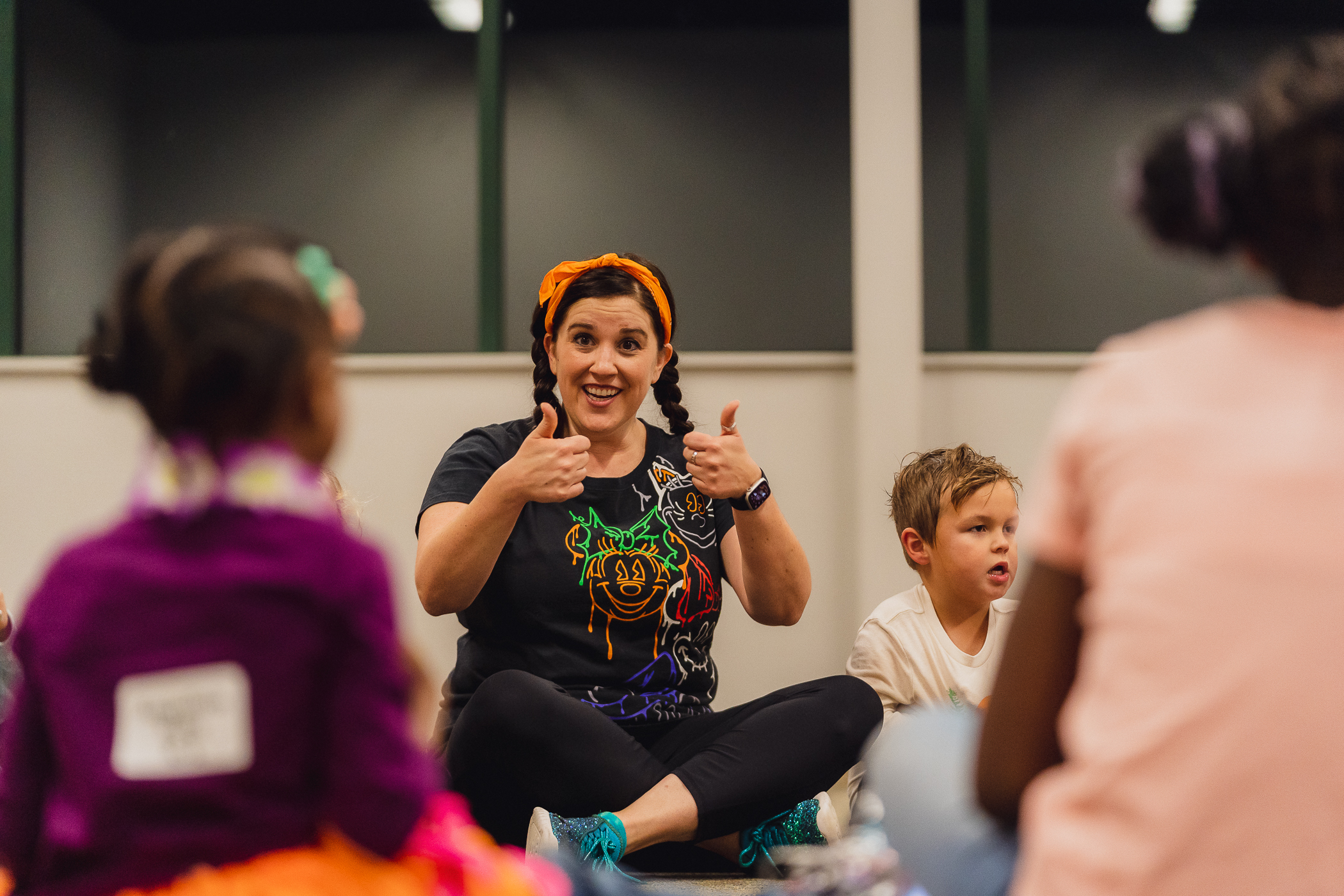 A Kazoo teacher gives two enthusiastic thumbs-up to a circle of young students