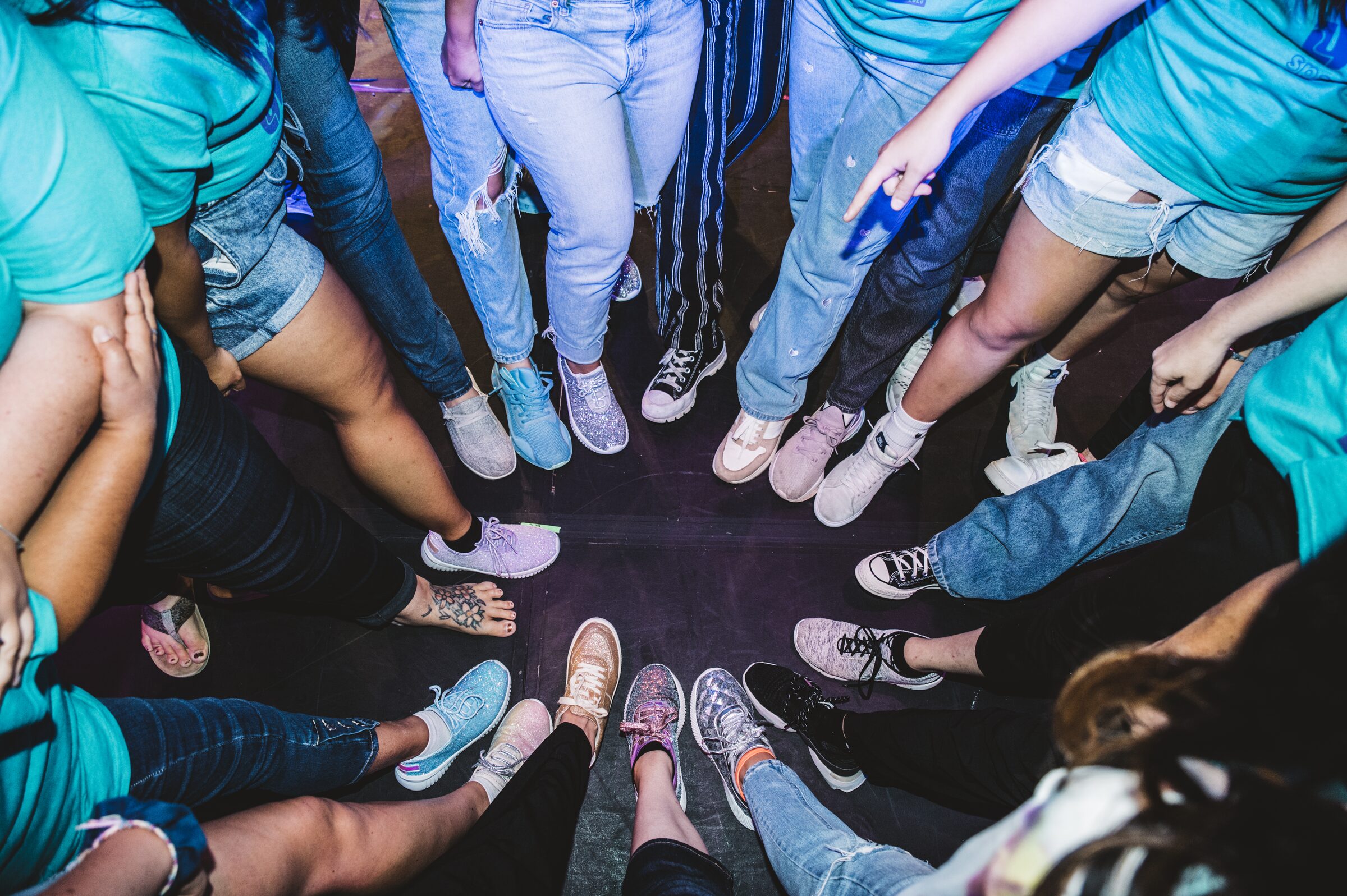 Overhead view of students standing in a tight circle, sneakers and sandals pointing inward toward a common center